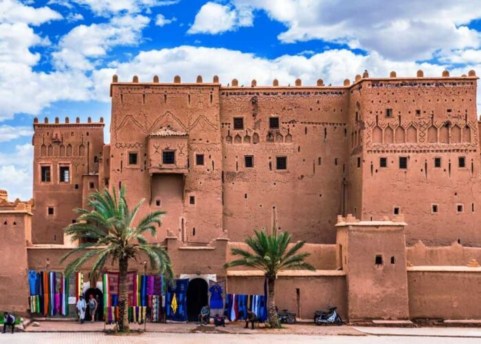 raditional Kasbah in Ouarzazate with colorful market stalls selling textiles under a bright blue sky, illustrating Morocco’s rich culture and historic architecture.