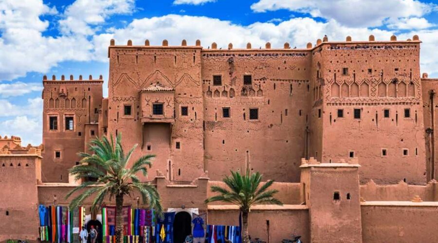 raditional Kasbah in Ouarzazate with colorful market stalls selling textiles under a bright blue sky, illustrating Morocco’s rich culture and historic architecture.